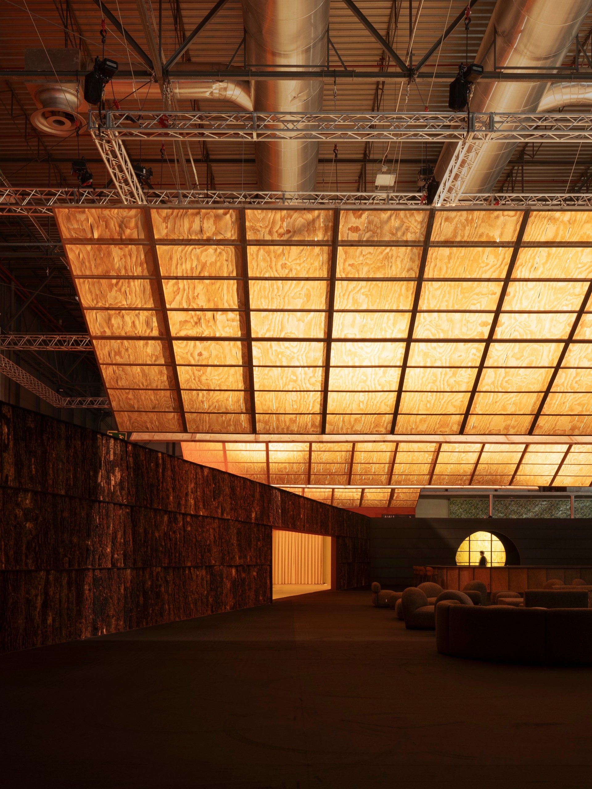 Wooden light planes glowing above a dark lounge with a lit restaurant opening at the far end