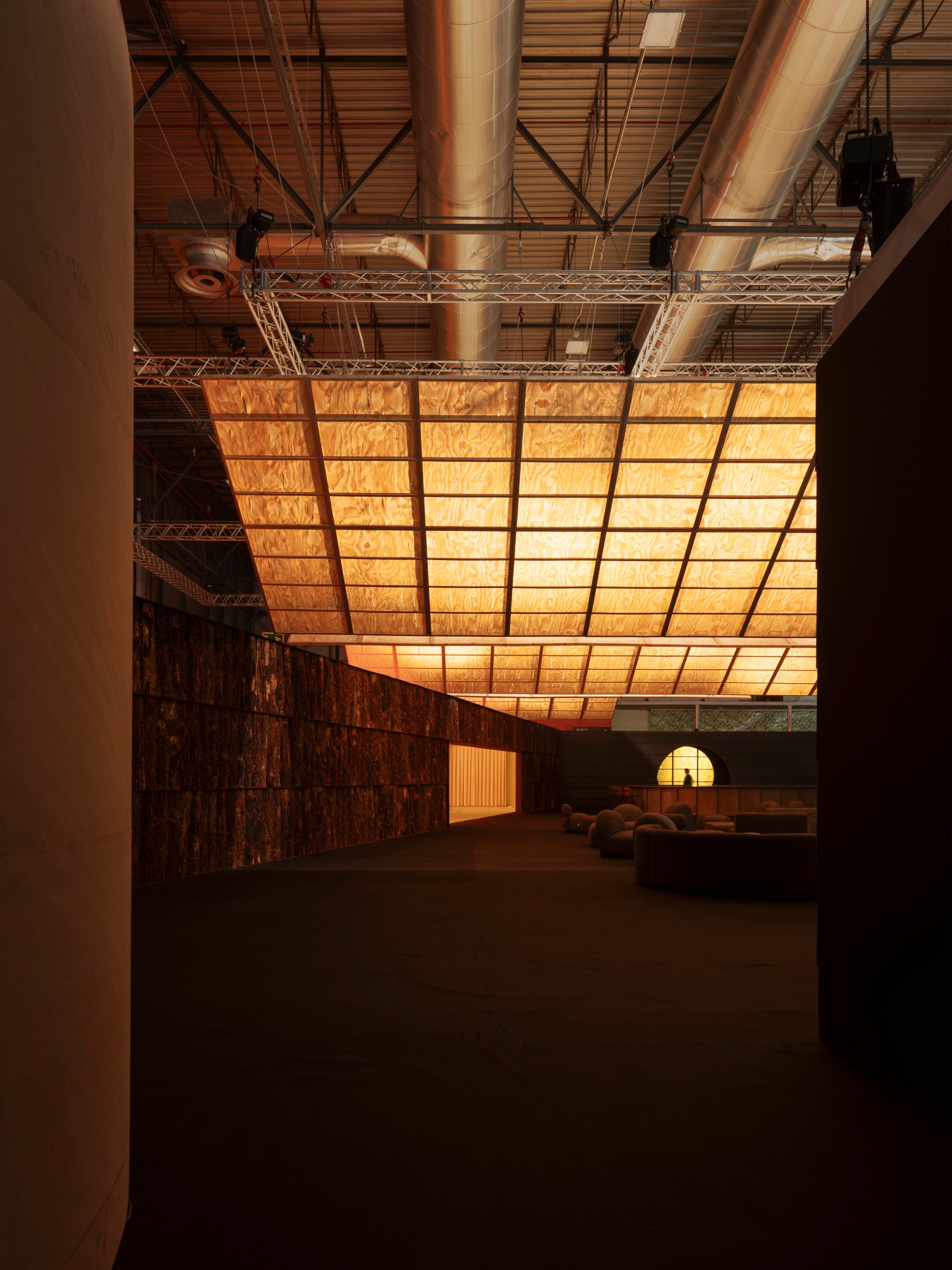 Dark bark-clad walls beneath suspended glowing timber planes