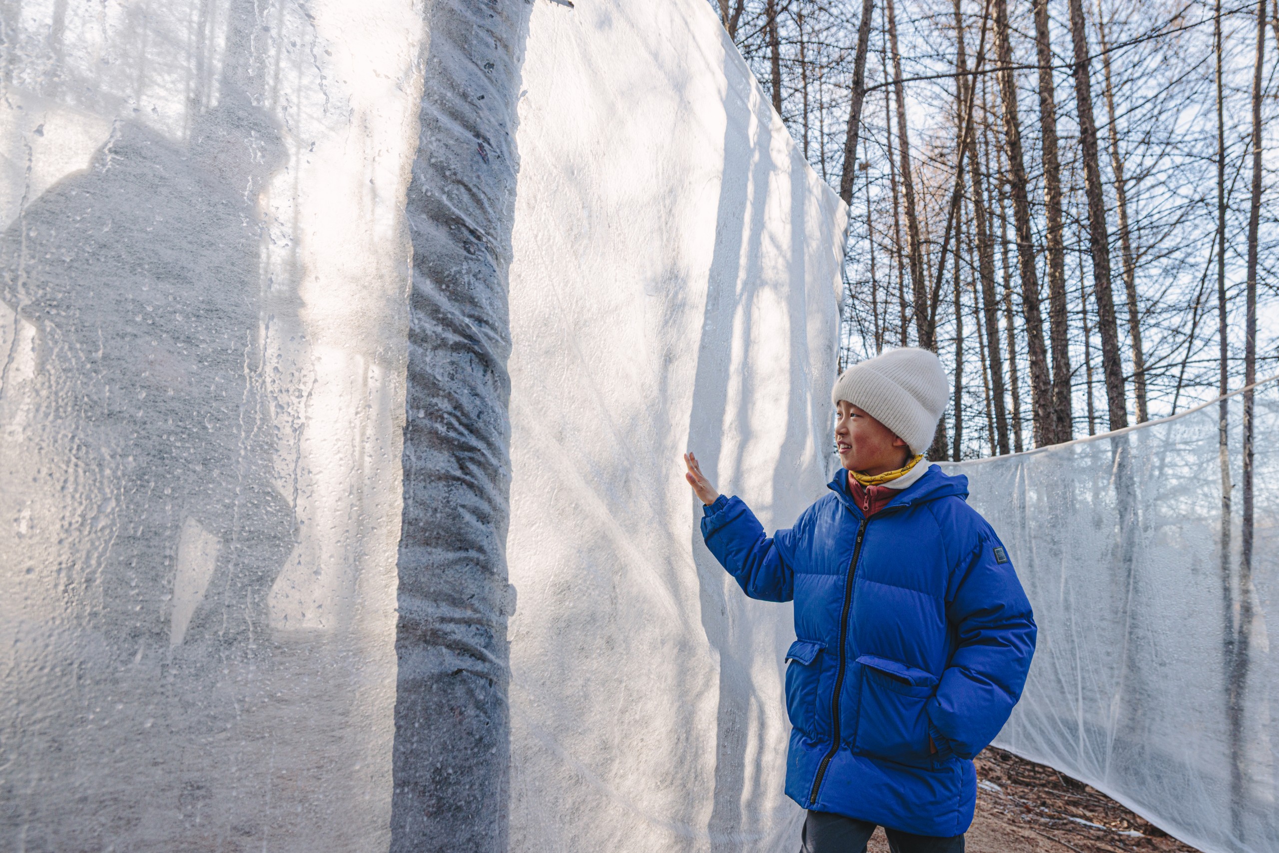A visitor in a blue jacket touching an ice wall as shadows fall across its surface