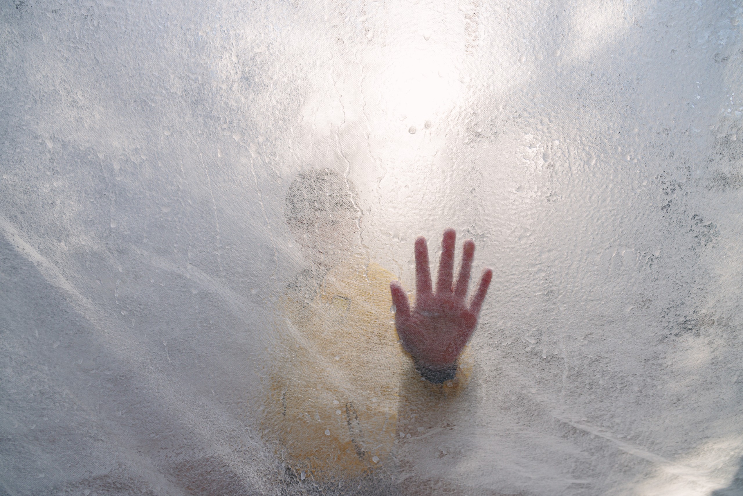 A hand pressed against an ice wall, seen blurred from the other side