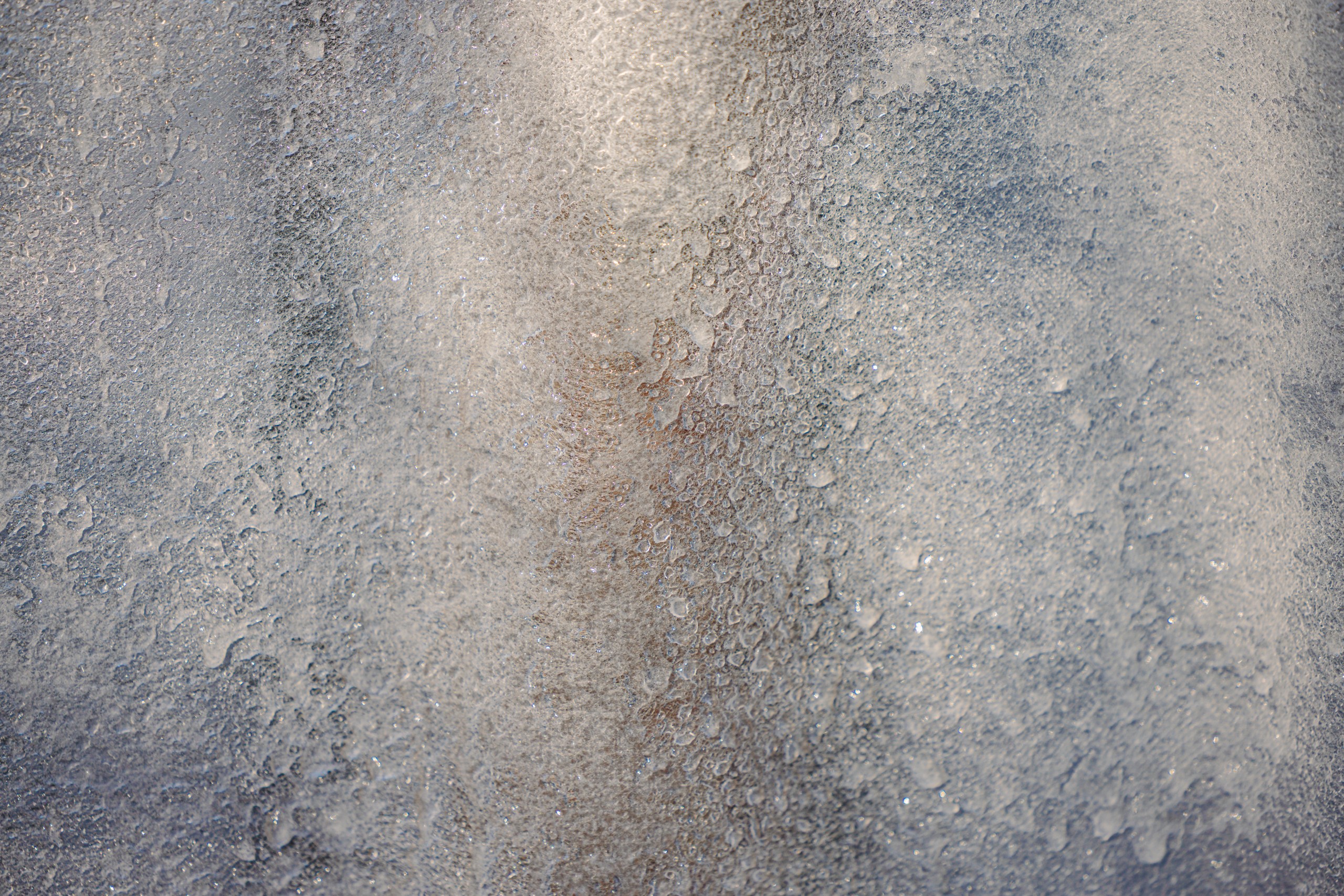 Detail of a textured ice surface with soft traces of colour and light