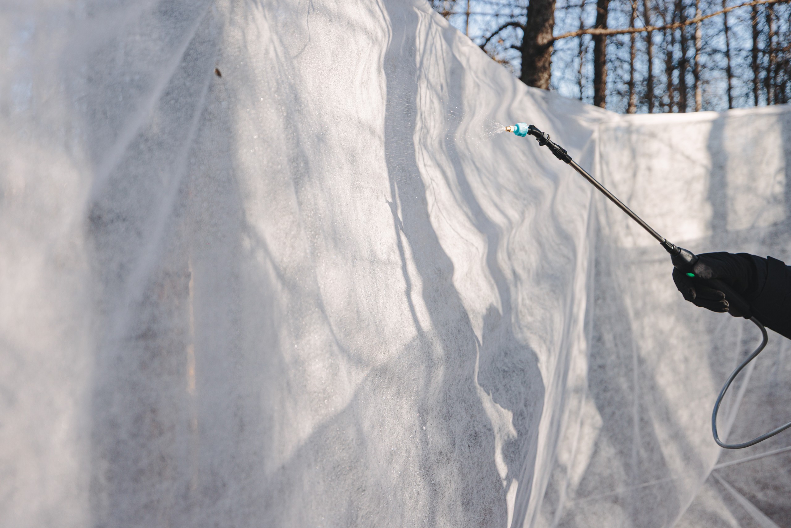 A gloved hand spraying water onto suspended fleece to form an ice wall