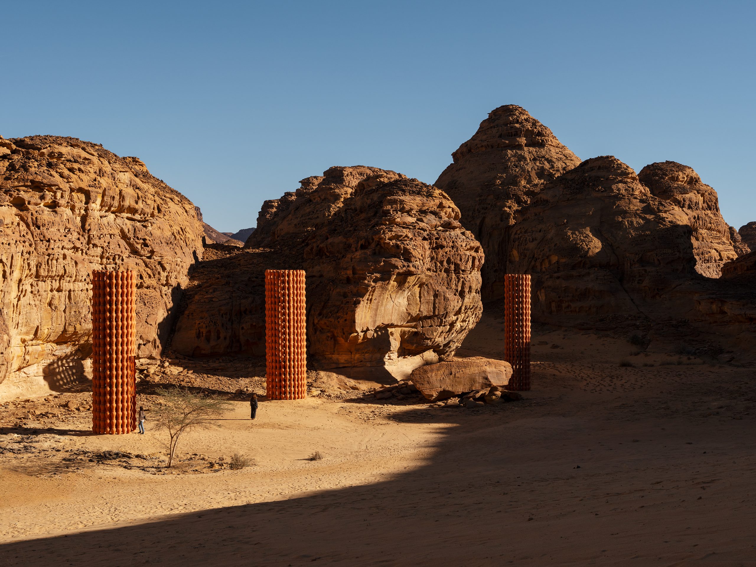 A wide view shows the earth-jar towers set within the desert landscape of AlUla.
