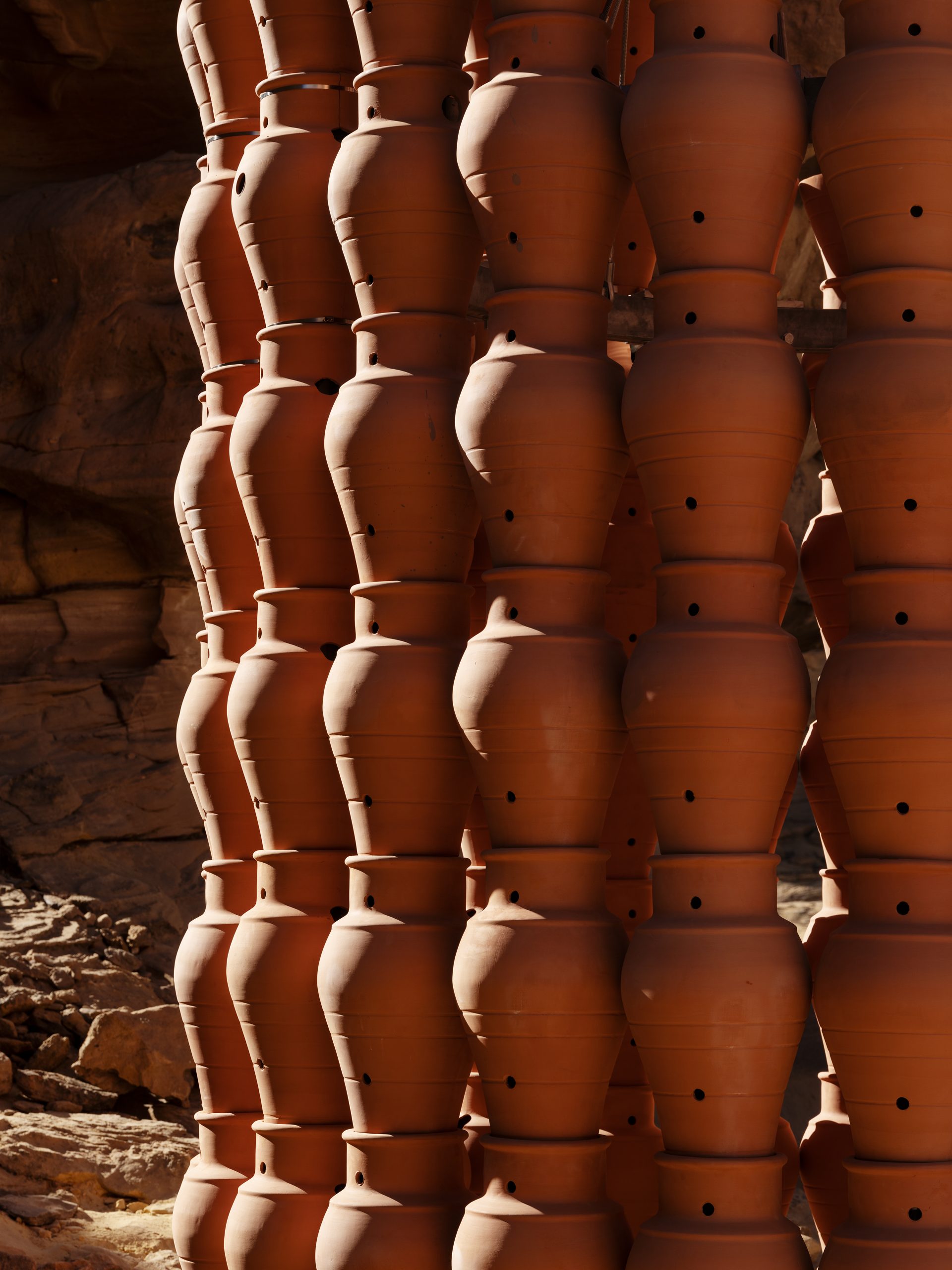 Hand-cut apertures interrupt the clay surfaces and cast changing shadows around the work.