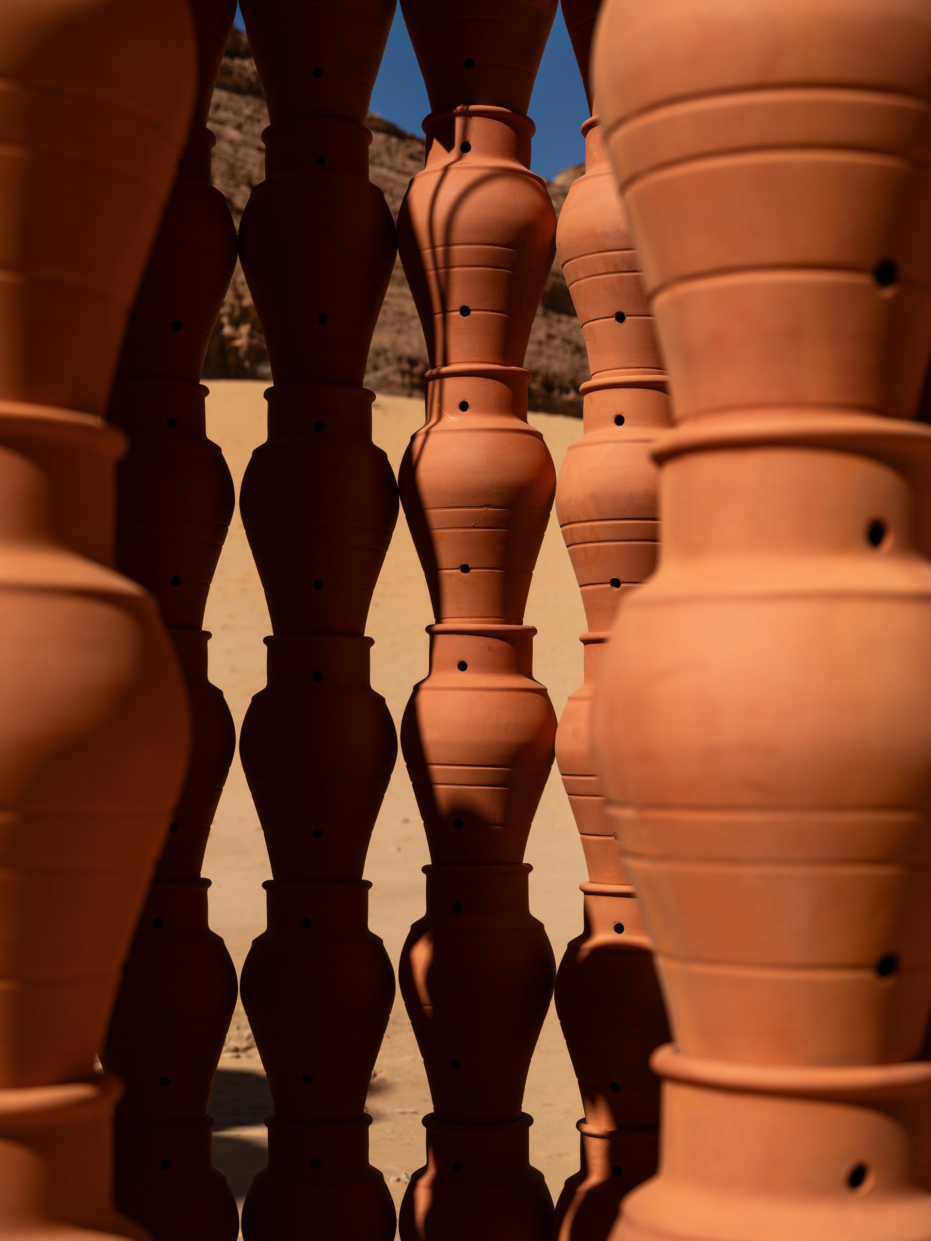 The jars’ open pattern frames fragments of the AlUla landscape beyond.