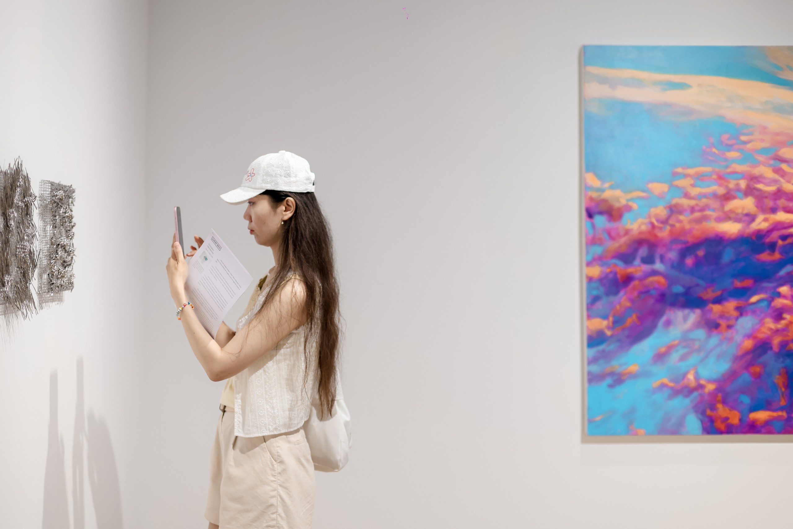 A visitor photographs a cloud painting in pink, blue and violet