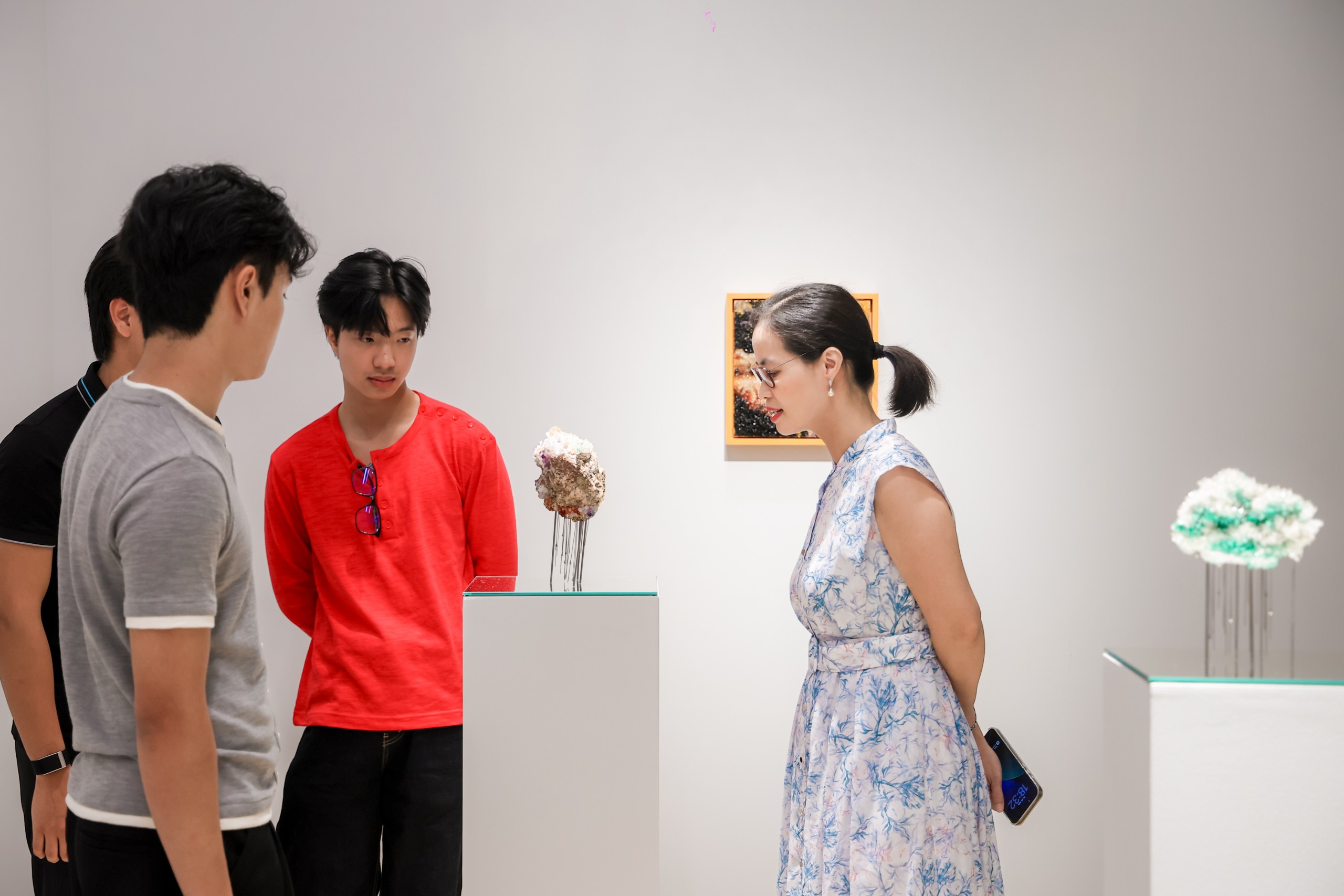 Visitors stand near small sculptures on white plinths