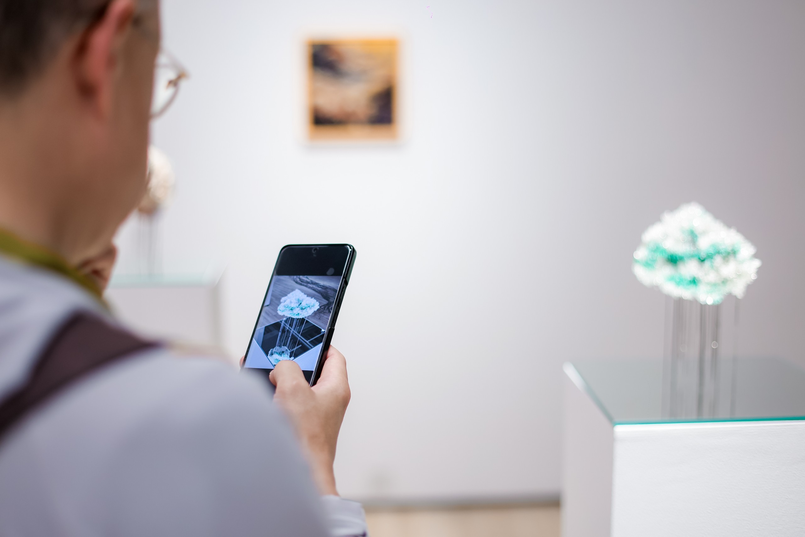 A visitor photographs a pale cloud-like sculpture on a glass plinth