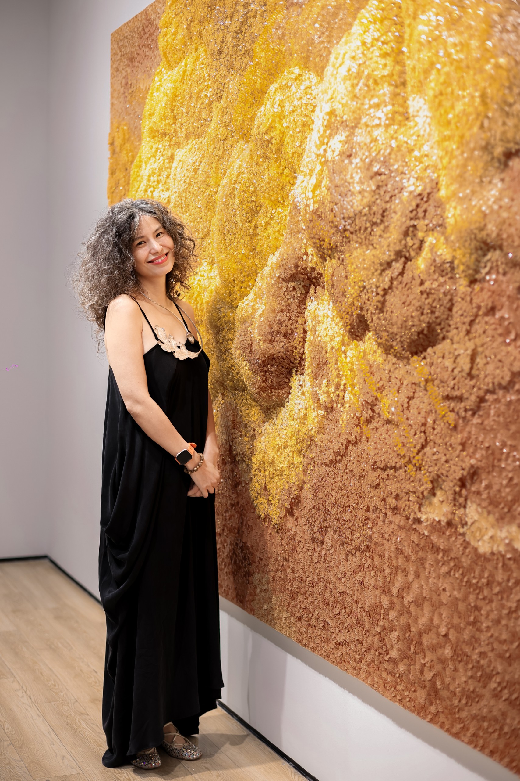 A woman beside the textured golden surface of the beaded work