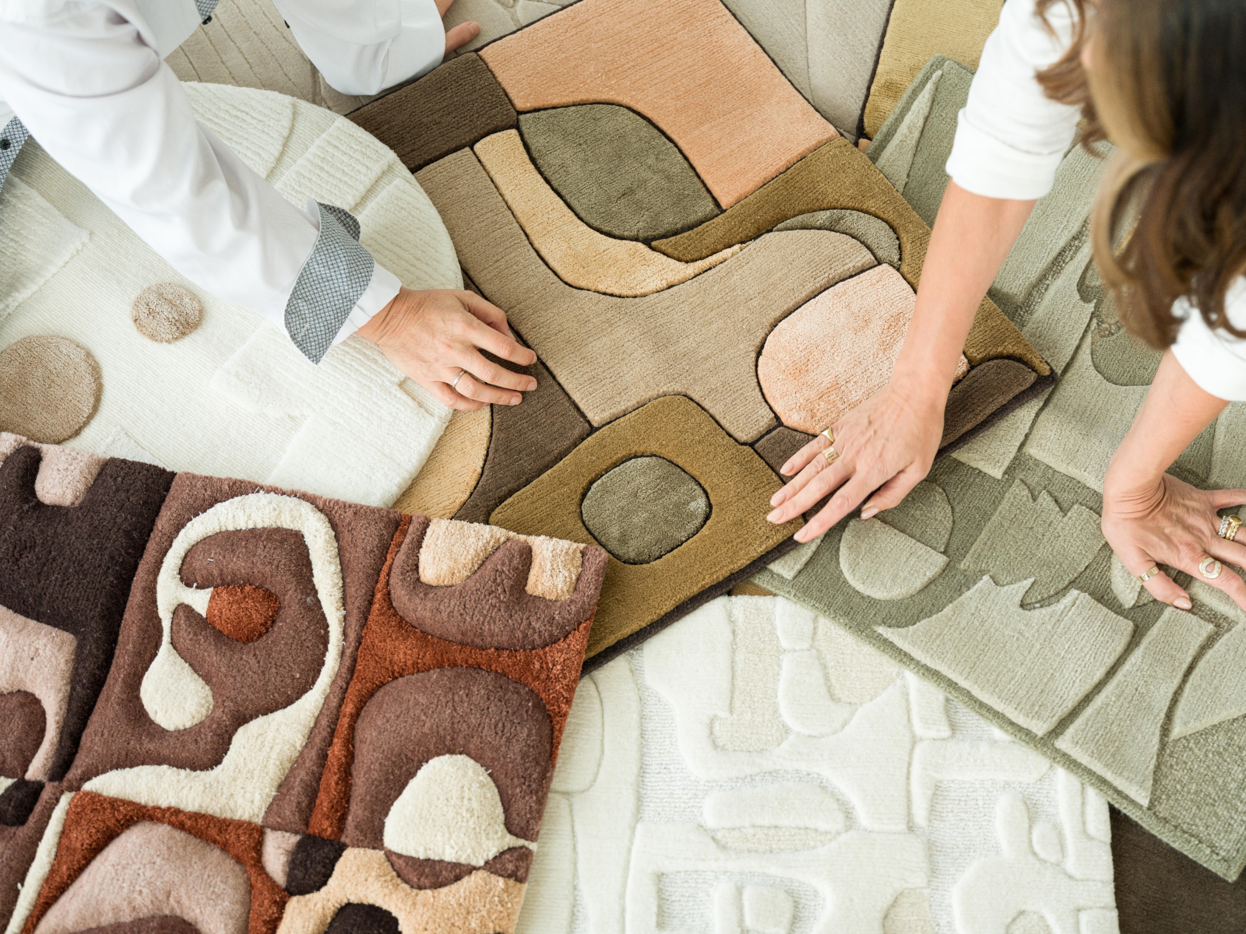 Hands arranging several rugs from the collection