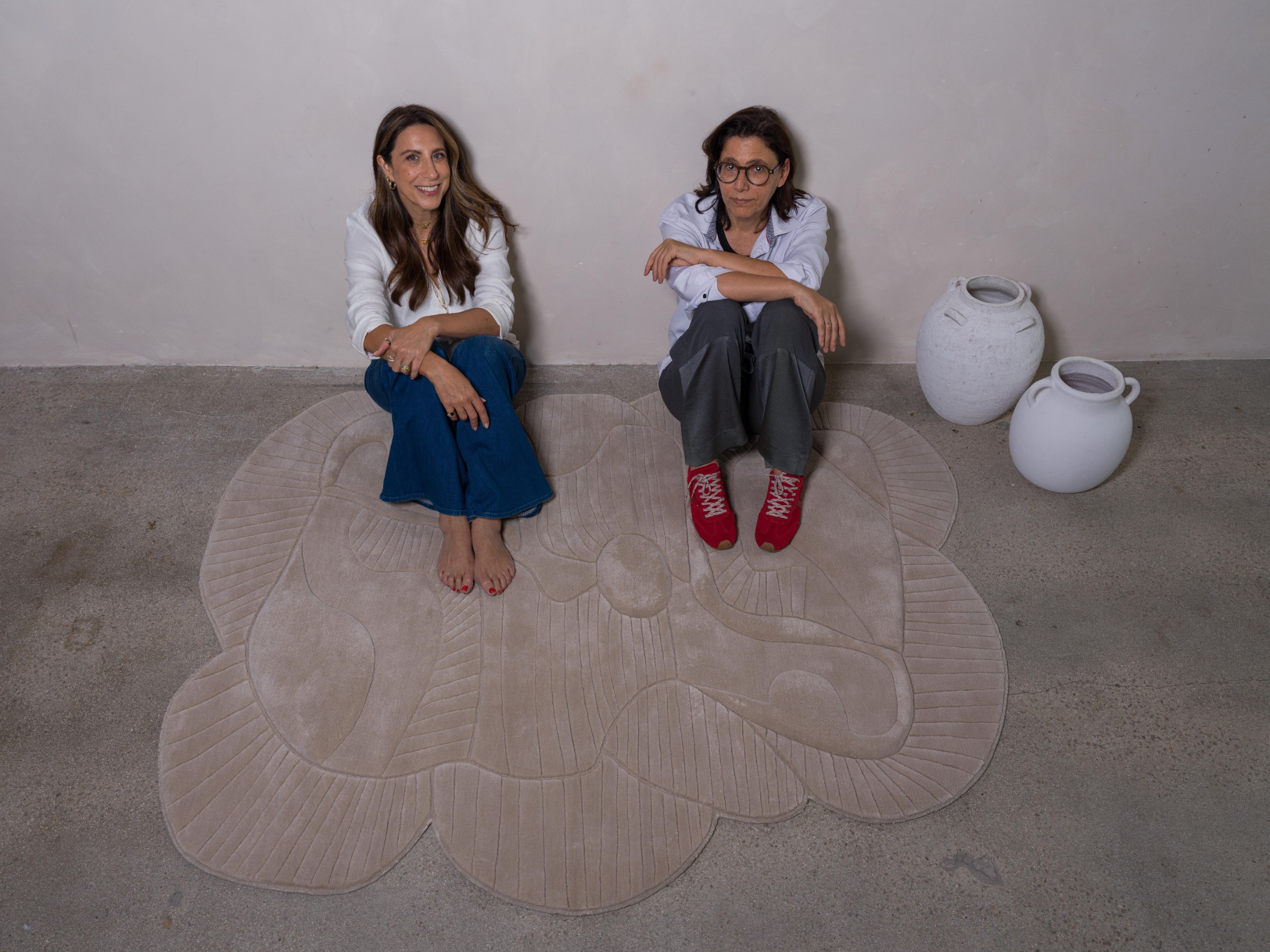 Two women seated on a cream rug with ceramic vessels
