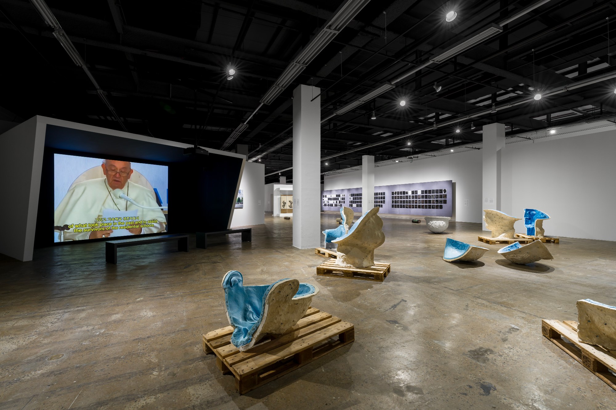 Gallery 3 with a video screen and sculptures on pallets