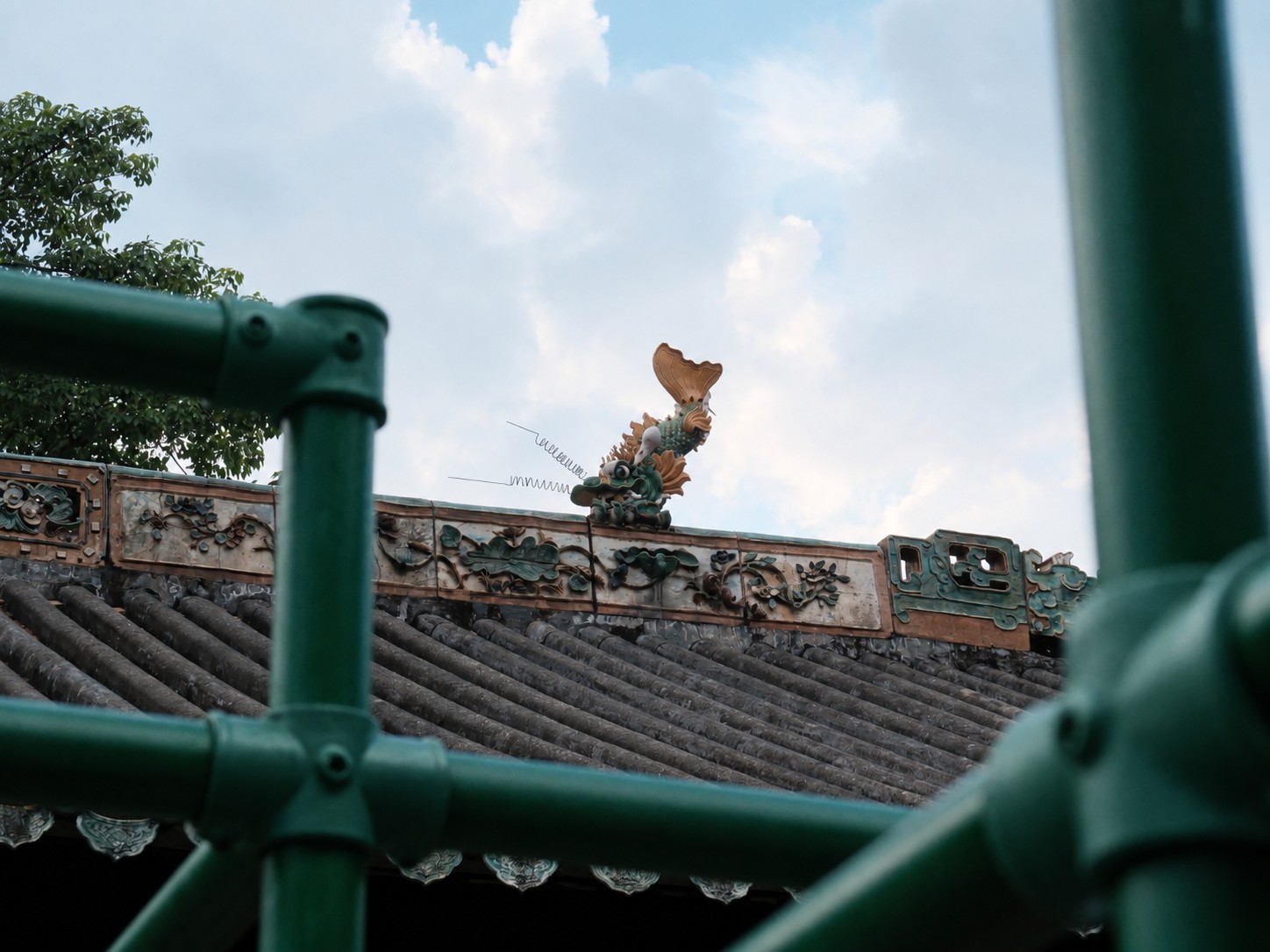 The green of the scaffolding echoes the ceramic ornaments on the roof