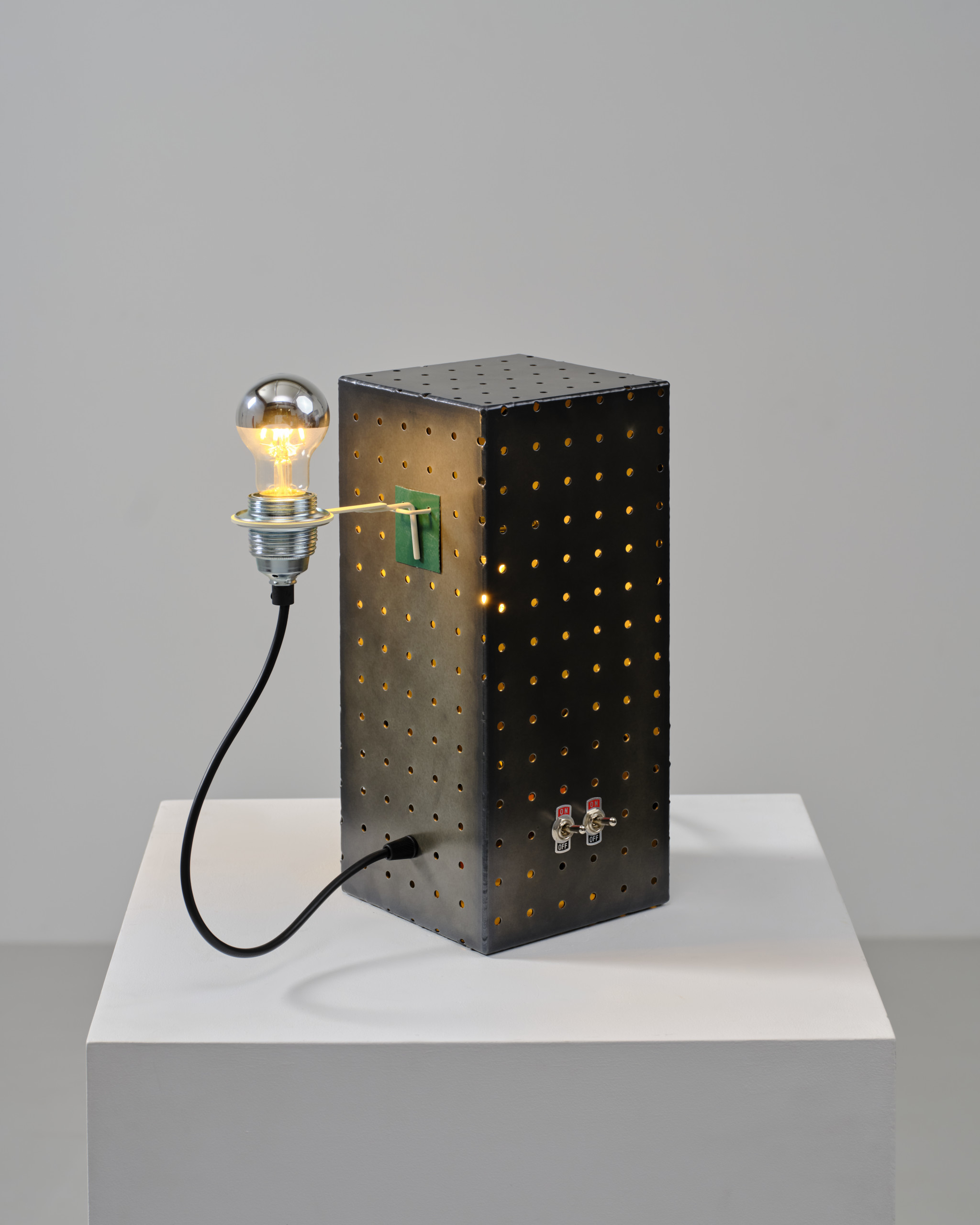 Black pegboard table lamp with light through its holes