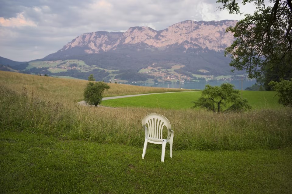 A white monobloc chair alone in a mountain meadow