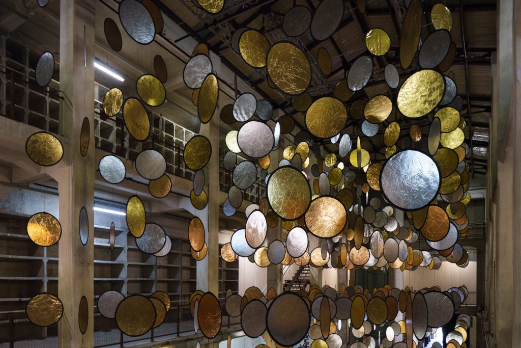 SpY, HALOS, gold and silver reflective circles suspended in a former railway factory in Florence